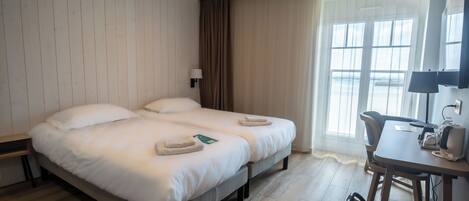 Una habitación de hotel con una cama grande, un escritorio con silla y una ventana con cortinas.