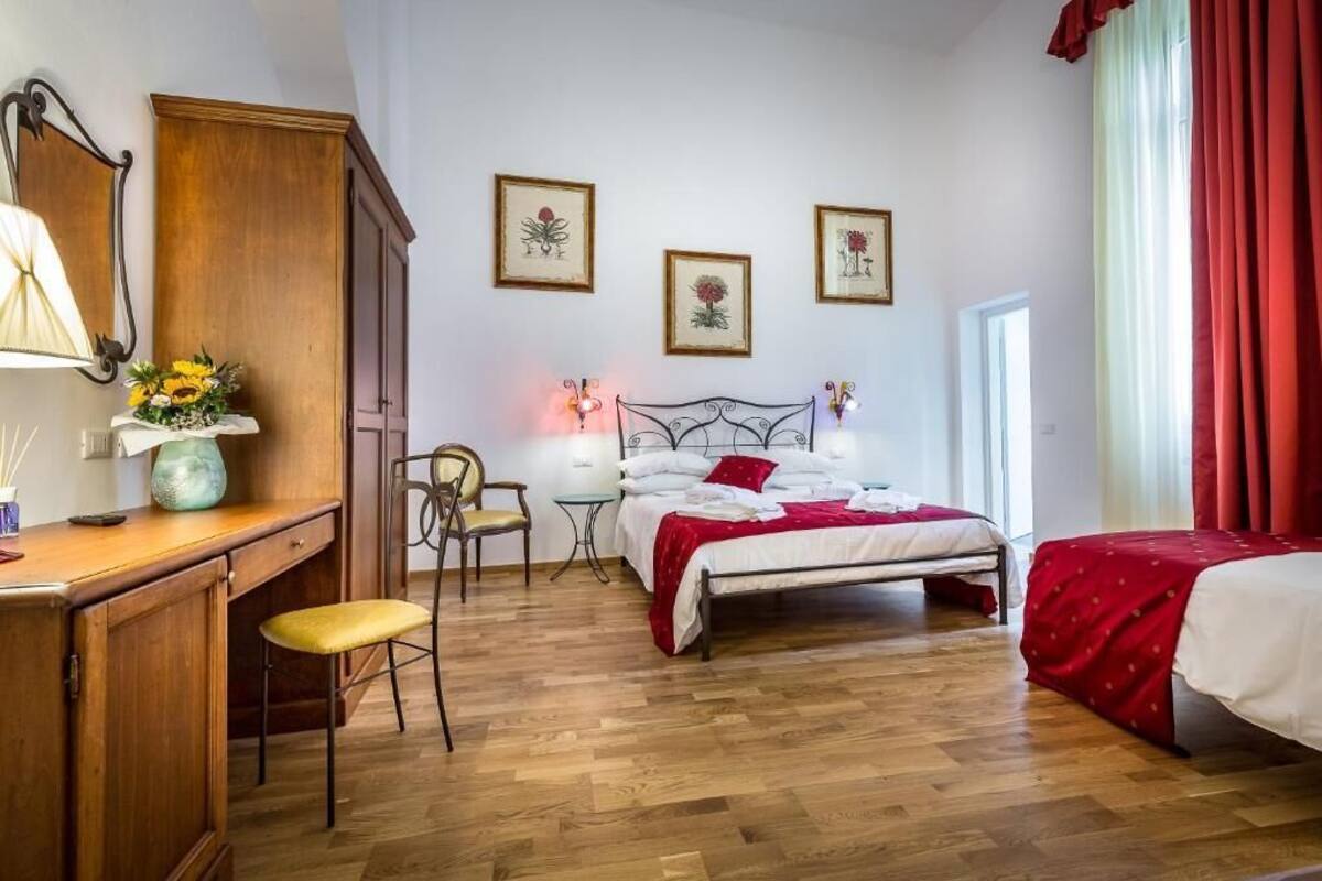 A bedroom with a wooden desk, a chair, a bed with red bedding, and two framed pictures on the wall.