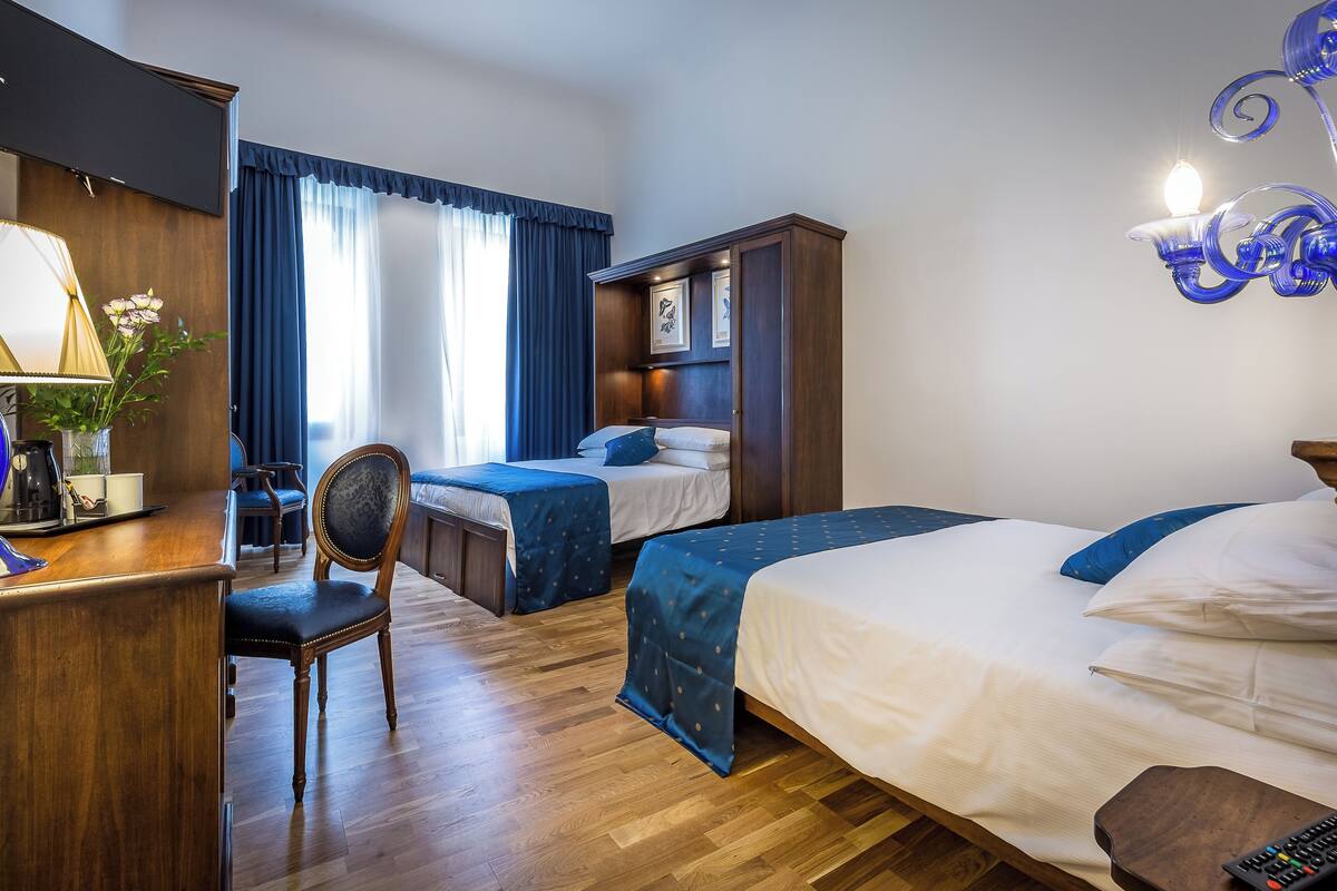 A hotel room with two beds, a desk with a lamp, a chair, and a dresser.