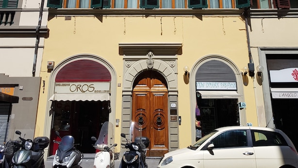 A building with a yellow facade, multiple windows with shutters, and a central entrance with a wooden door.