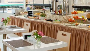 Montaje de un bufé de desayuno con gran variedad de alimentos, una estación de café y flores decorativas.