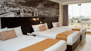 Habitación de hotel con tres camas, un ventanal con vistas a la ciudad y un mural en la pared.