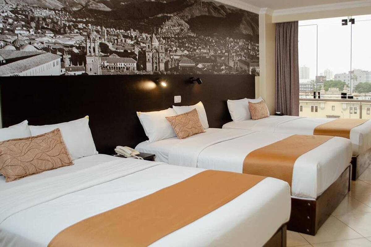 Habitación de hotel con tres camas, un ventanal con vistas a la ciudad y un mural en la pared.