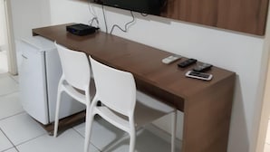 A compact room with a wooden desk, a white chair, a small white refrigerator, and a mounted television. - Pousada Tambau Familly (João Pessoa)