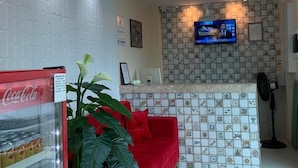 A reception area with a red sofa, a large plant, a Coca-Cola refrigerator, a television, and a patterned tile backsplash. - Pousada Tambau Familly (João Pessoa)