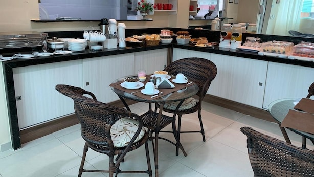 A modern kitchen with a central island, wicker chairs, and a dining table set for four. - Pousada Tambau Familly (João Pessoa)
