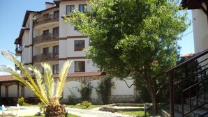 Un chemin menant à un immeuble à plusieurs étages doté de balcons, entouré de verdure et de plantes en pot.