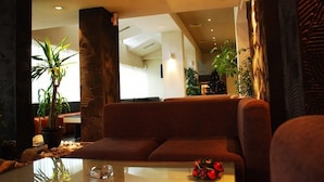Un hall d’hôtel moderne avec un canapé marron, une table en verre et des plantes en pot.