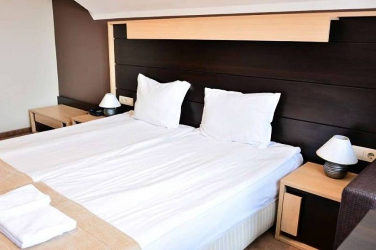 Une chambre d’hôtel avec un grand lit, deux tables de chevet et une petite table de nuit avec une lampe.