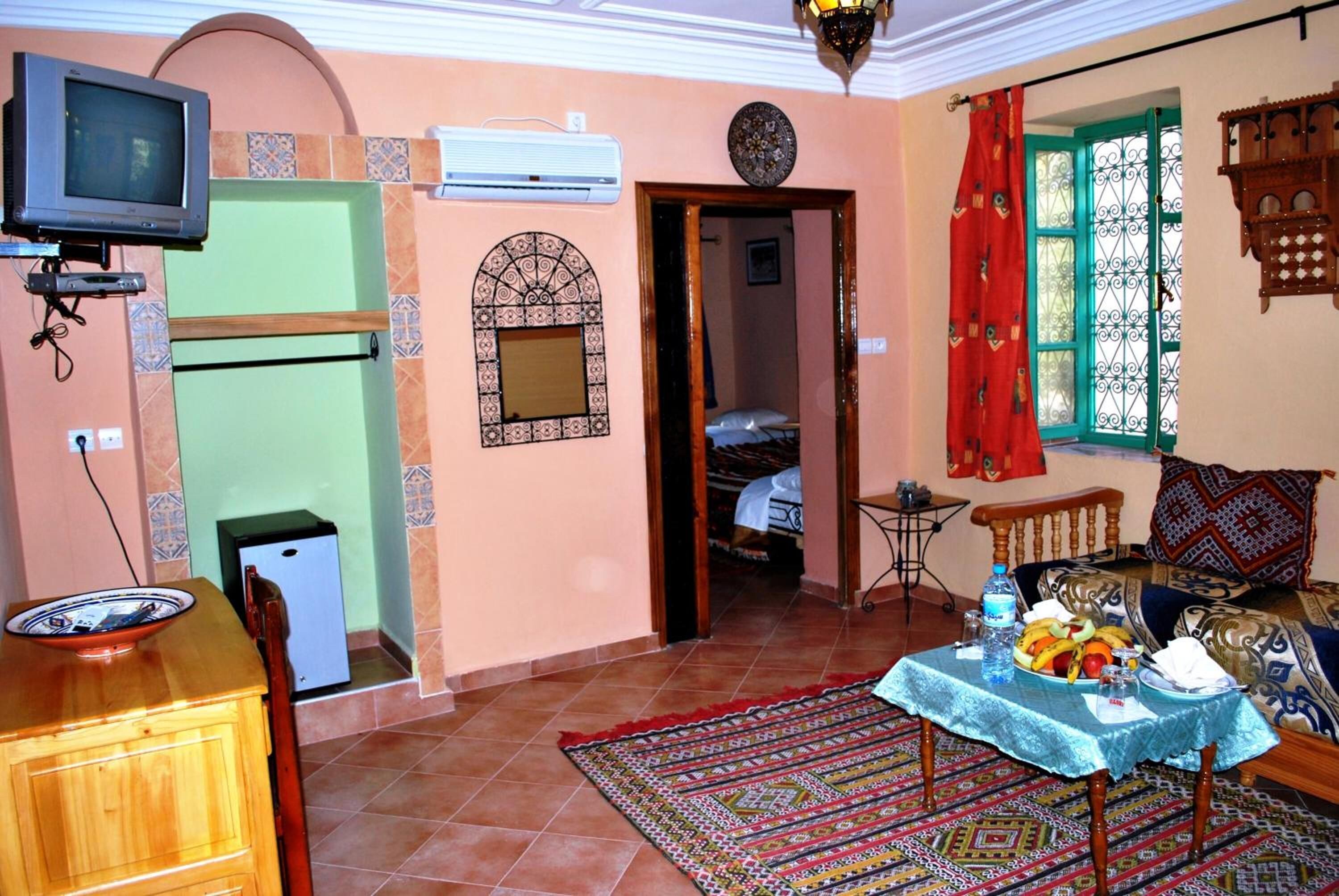 Una sala de estar con televisor, una mesa de comedor con un bol, un sofá y un tapete estampado.