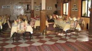 Un espace repas avec un sol à carreaux, des tables disposées pour accueillir plusieurs personnes et un plafond en bois rustique.