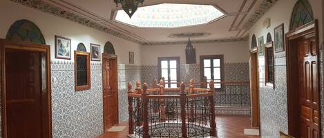 Una habitación con una mesa de madera en el centro, rodeada de sillas, paredes con diseño y un tragaluz.