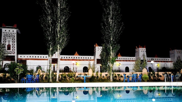 Vue nocturne d’un hôtel qui ressemble à un château, avec une piscine en premier plan.