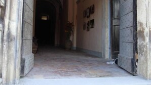 Um corredor com tetos abobadados e paredes de pedra. Há quadros nas paredes e uma porta à direita.