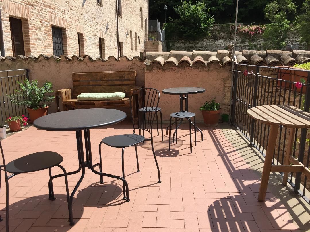 An outdoor patio with brick flooring, a wooden bench, metal tables and chairs, and potted plants.