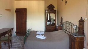 Quarto com cama, cómoda de madeira, espelho, cadeira e porta de madeira.