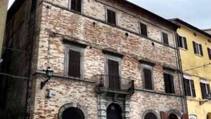 Um edifício de dois andares com fachada de pedra, várias janelas e uma entrada central com varanda.