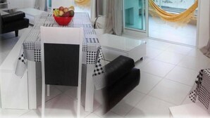 A modern living room with a dining table, black sofa, and a view of the city through large windows. - Tu Casa De La Playa Florianópolis Brasil (Florianópolis)