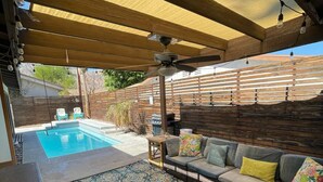 Un espacio al aire libre techado con piscina, techo de madera y un sofá con cojines.
