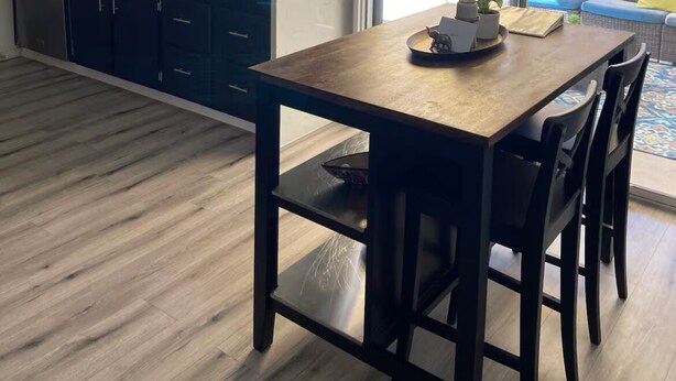 Una cocina moderna con armarios oscuros, una mesa de comedor de madera y vista al patio trasero a través de una puerta corrediza de vidrio.
