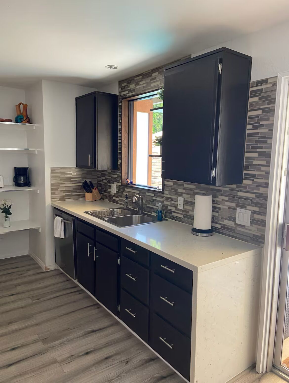 A modern kitchen with dark cabinets, a large window, and a tiled backsplash.