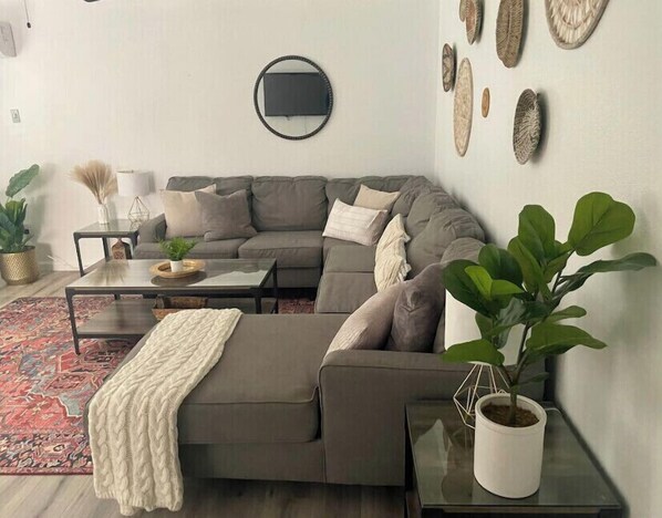 Un salon moderne avec un canapé d’angle gris, une table basse et une plante en pot.