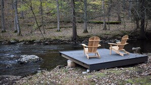 Une jetée en bois avec deux chaises Adirondack donnant sur une rivière, dans une zone boisée.