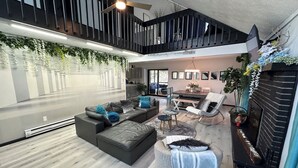 Un salon moderne avec un canapé d’angle, un pouf rond et un coin repas comprenant une table et des chaises.