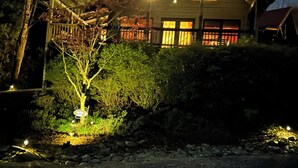 Una cabaña de madera con un porche, un pequeño jardín y un camino de entrada de grava.