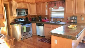 Una cocina con armarios de madera, microondas, estufa, lavavajillas y fregadero.