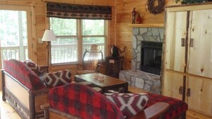 Interior acogedor de una cabaña con chimenea de piedra, muebles de madera y vistas al exterior.