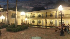 Un patio de hotel con piscina, mobiliario exterior y un edificio de dos plantas con balcones.