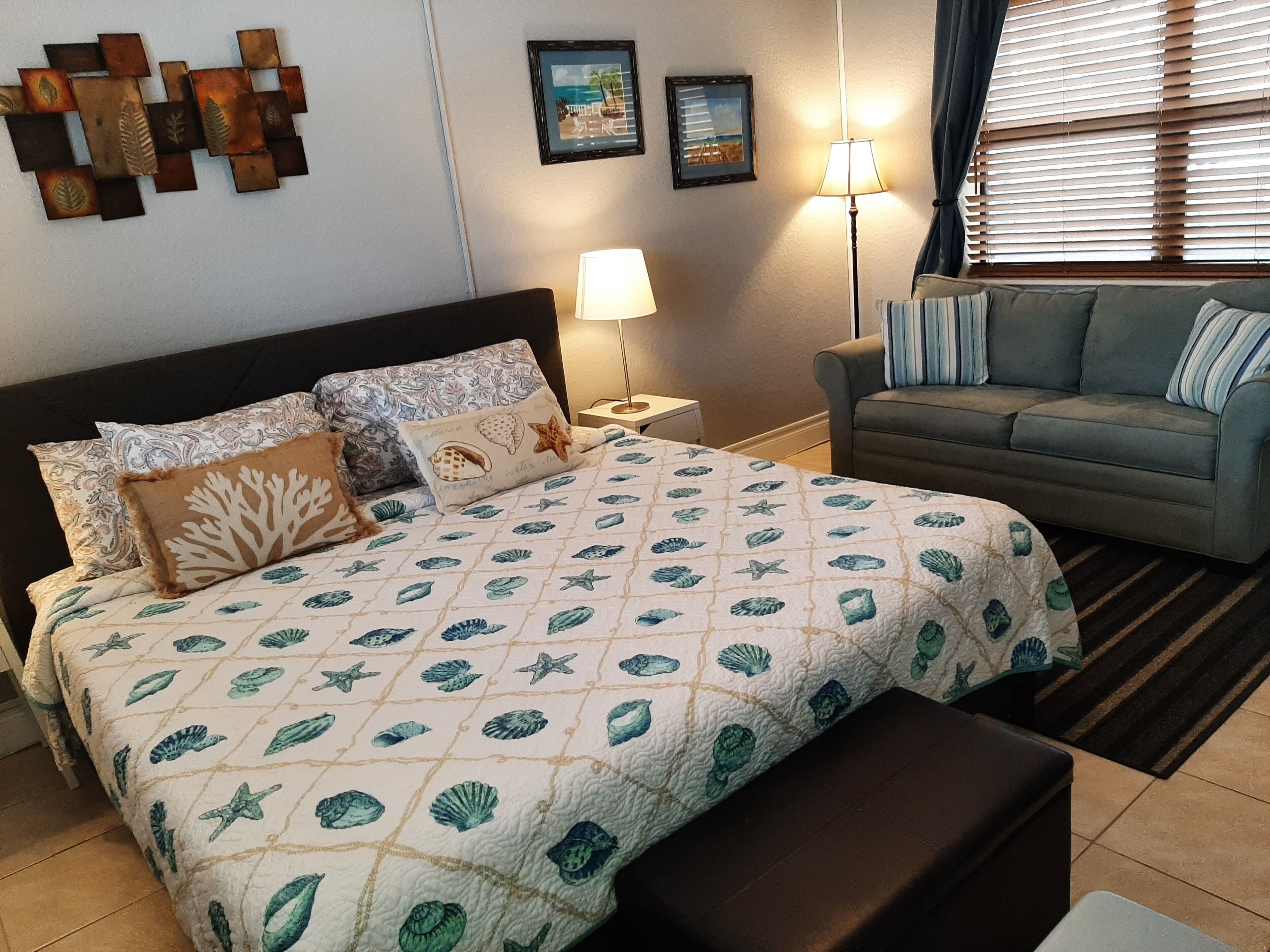 Una camera da letto con un letto, un comodino, una lampada, un divano e una finestra con persiane.