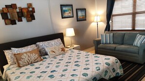 Un dormitorio con cama, mesita de noche, lámpara, sofá y ventana con persianas.