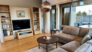 A modern living room with a flat-screen TV, wooden bookshelves, a brown sofa, and a round coffee table. - Luxury House with a Cozy Guesthouse + Hot Tub close to Snæfellsnes National Park (Borgarnes)