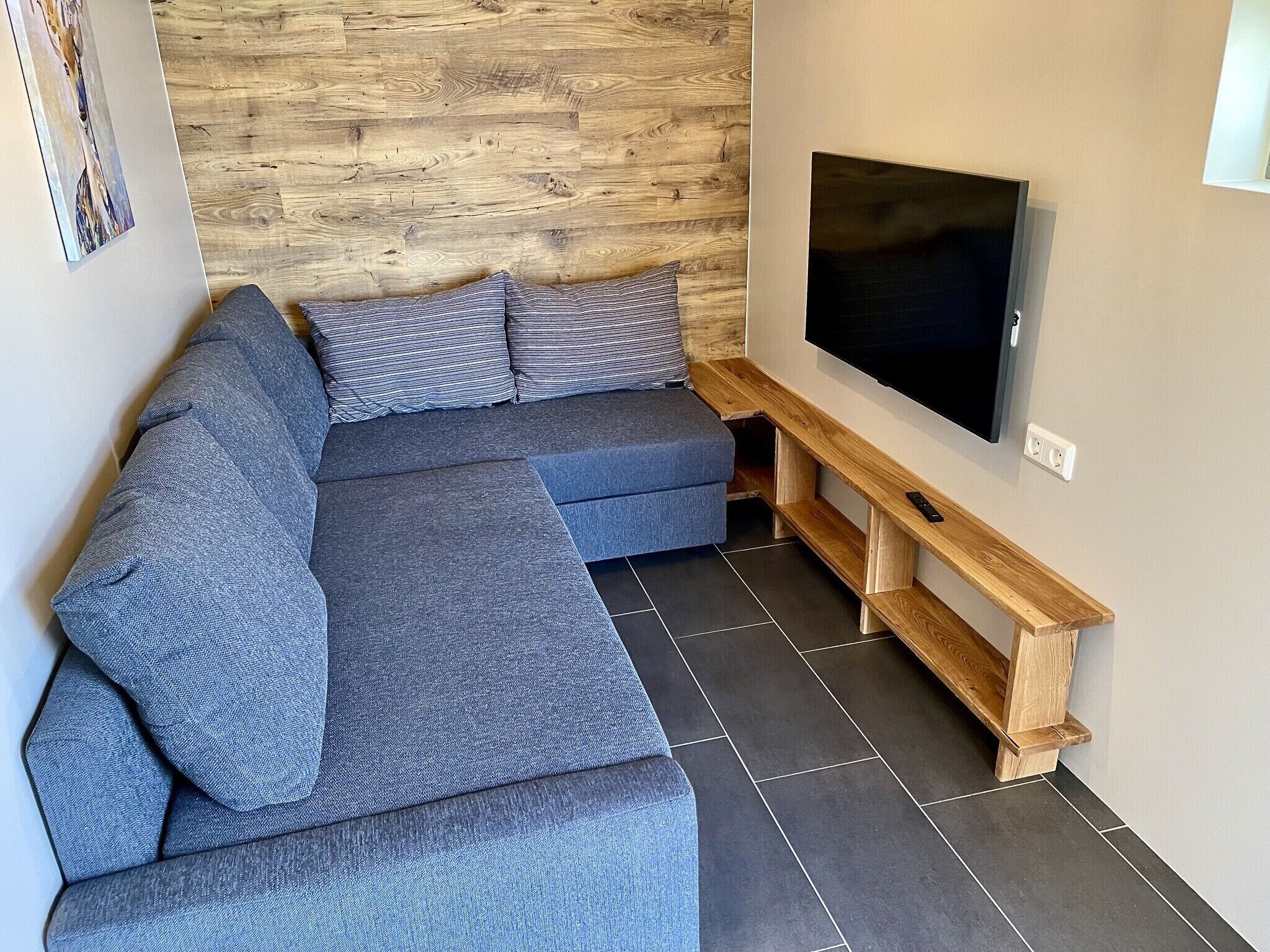 A modern living room with a sectional sofa, a flat-screen TV, and a wooden accent wall.