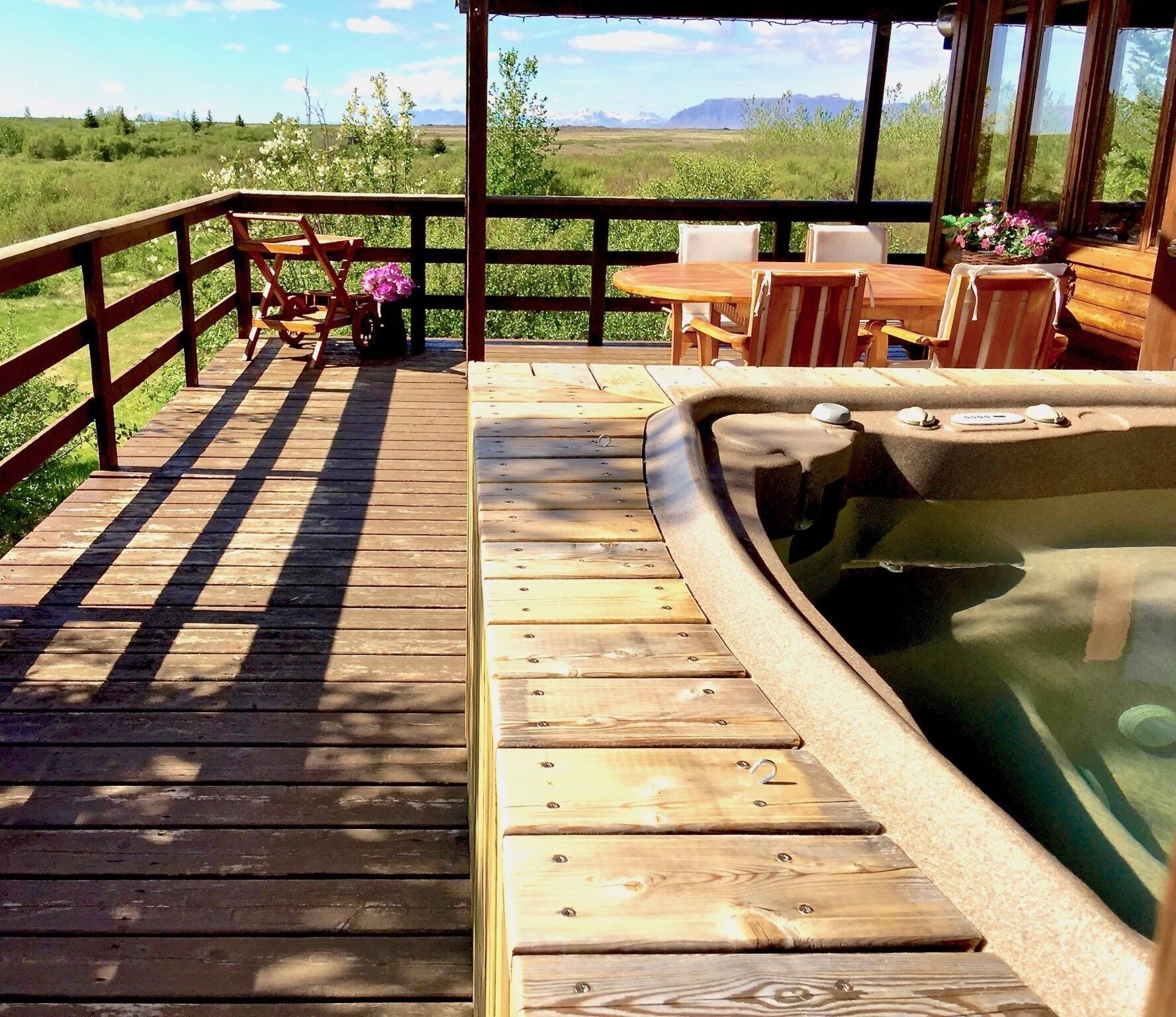 Una terraza de madera con un jacuzzi, mobiliario exterior y una vista panorámica.