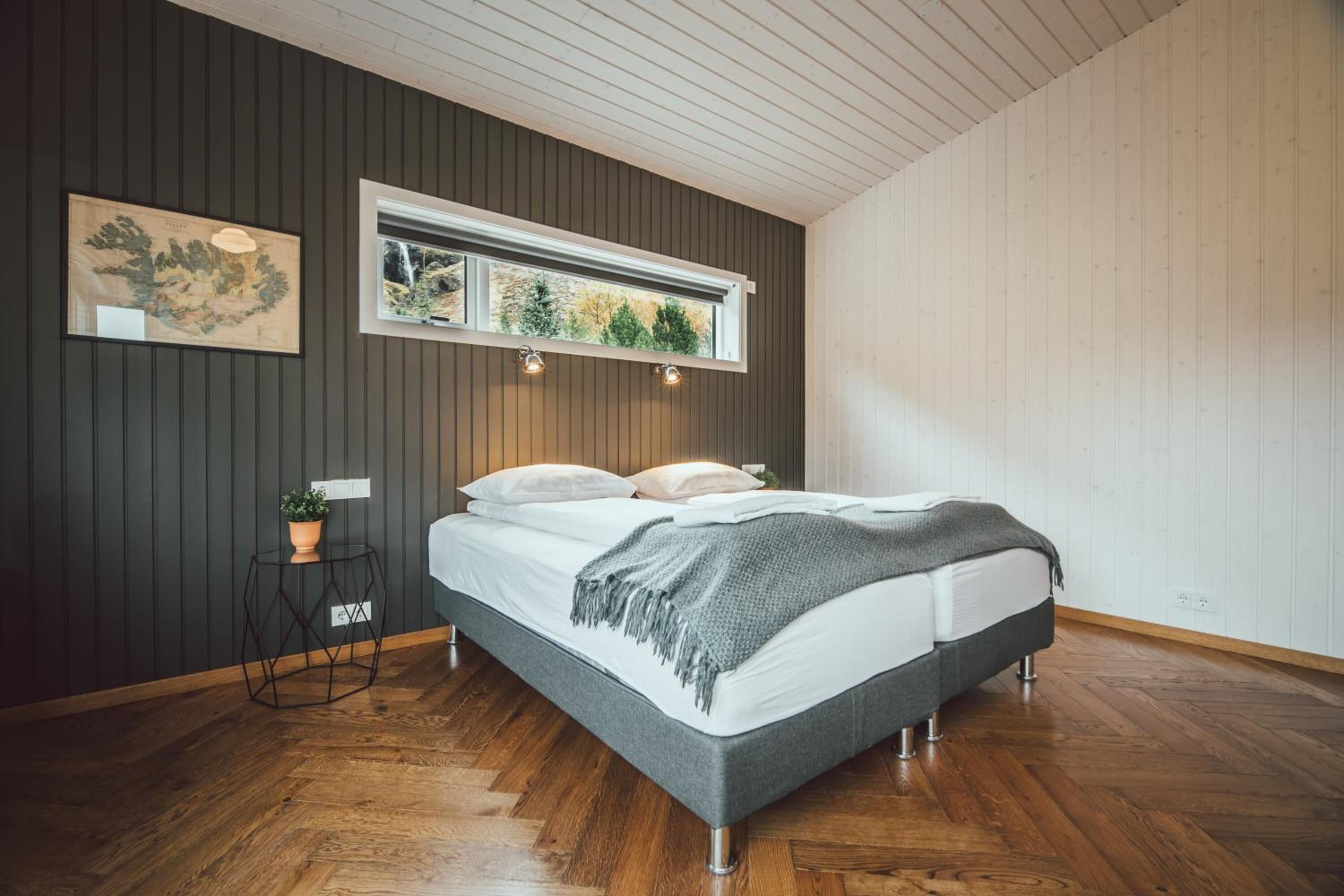 A bedroom with a bed, a window, a map, and a small table with a plant.