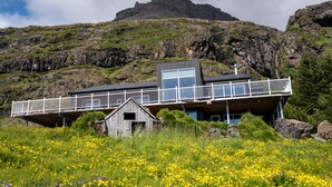 A modern building with a balcony overlooking a field of yellow flowers, set against a mountainous backdrop. - Ekra Glacier Lagoon (Reynivellir)