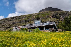 A modern building with a balcony overlooking a field of yellow flowers, set against a mountainous backdrop.
