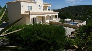 Une maison à deux étages avec une piscine, entourée de verdure et de collines.