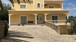 A two-story yellow building with a tiled roof, a stone wall, and a paved courtyard. - Beautiful villa, with private pool, set in hills with spectacular views  (Loule)