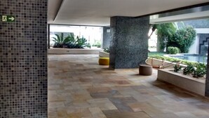Een ruime lobby met een betegelde vloer, een centrale kolom en een zithoek met een bank en een kleine tafel.