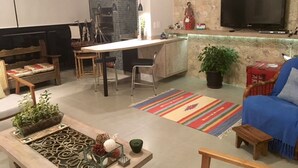 Een moderne woonkamer met een bank, een salontafel met decoratieve objecten, een eethoek met stoelen en een tafel, een keuken met een aanrecht en apparatuur, en een televisie aan de muur.