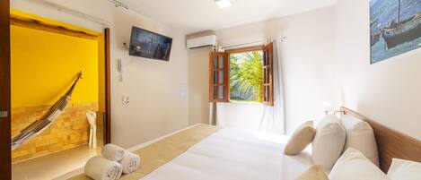 A hotel room with a bed, pillows, a hammock, a television, and a window with curtains.