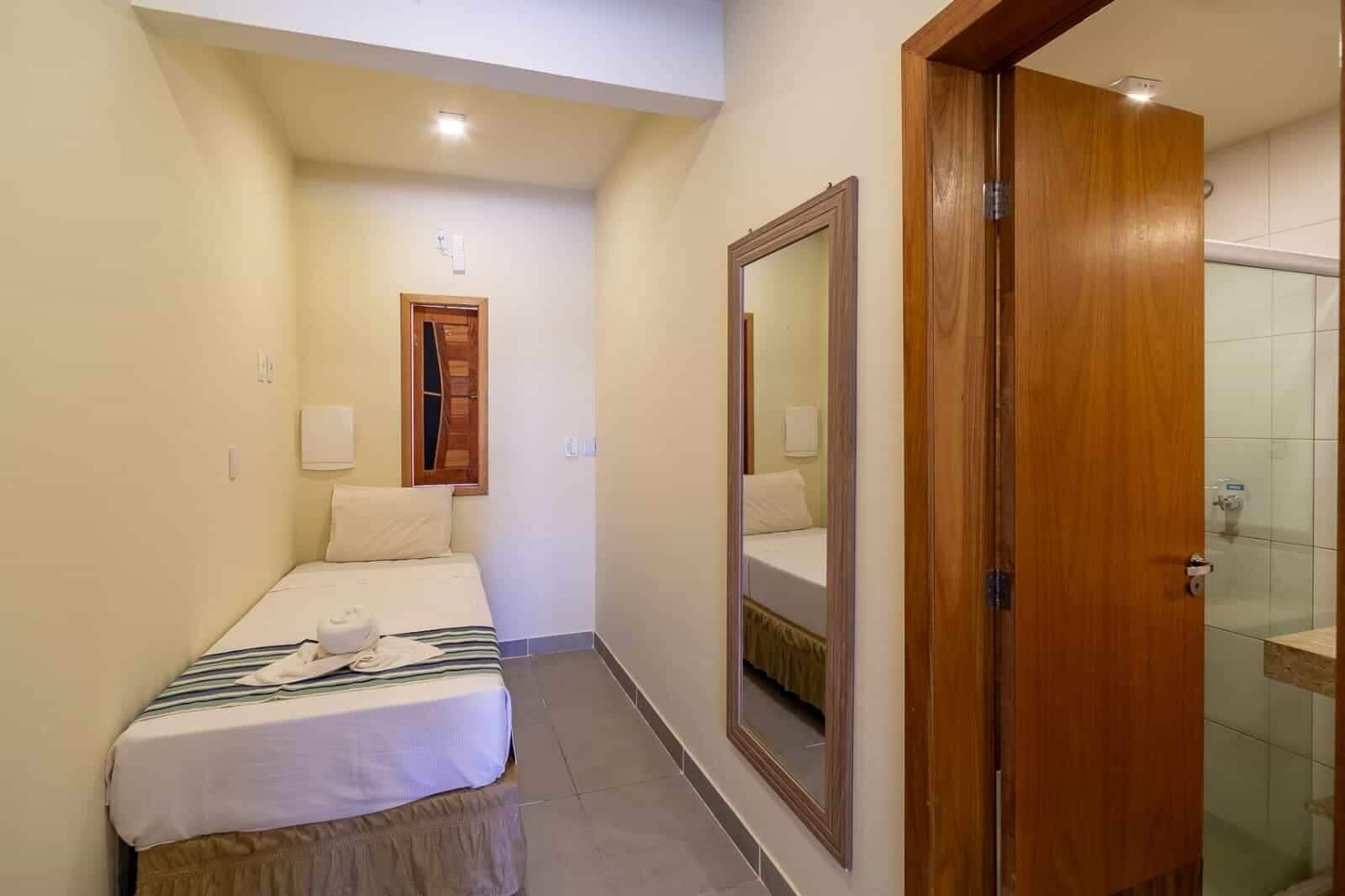 Una habitación de hotel con cama, espejo, puerta de madera y zona de ducha.