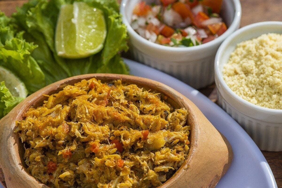 A wooden bowl filled with a shredded food dish, accompanied by a side of diced vegetables and a lime wedge.