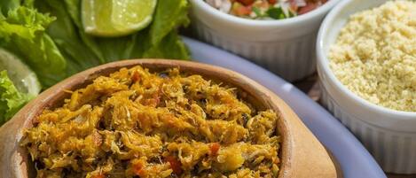 A wooden bowl filled with a shredded food dish, accompanied by a side of diced vegetables and a lime wedge.