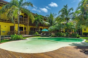 A resort with a pool, wooden deck, and tropical plants. - Pousada Tropicarim (Camaçari)
