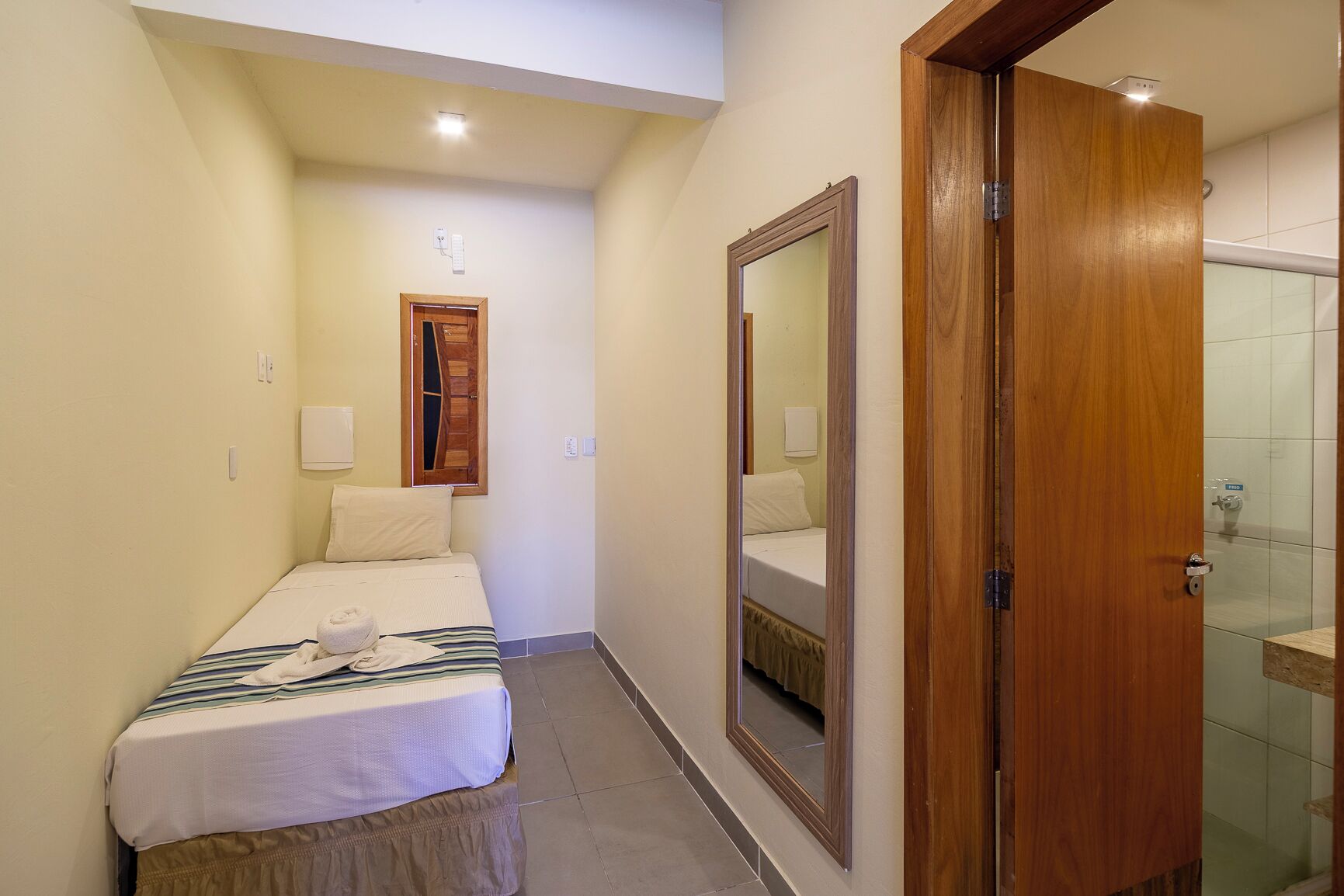 A hotel room with a bed, a mirror, a wooden door, and a shower area.